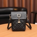 Black quilted crossbody bag with golden cat-head clasp and pearl pendant on a wooden table - Black