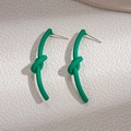 Détail de boucles d'oreilles nœuds verts à finition mate sur fond blanc texturé - Vert