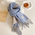 Flat lay of a two-tone light blue and beige scarf with tassels and decorative label - Blue Gray