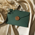 Détail d'une enveloppe vert foncé avec sceau en cire brune sur fond de soie champagne - Vert