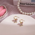 Détail de boucles d'oreilles papillon dorées avec cristaux roses sur plateau blanc - Papillon Rose