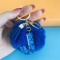 Detail of blue plush pompom and blue glitter resin letter J pendant on gold keychain - Letter J