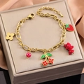 Detail of gold strawberry and cherry pendant bracelet on silk display padding - Bracelet