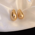 Détail de boucles d'oreilles goutte dorées sur tissu de soie avec éclat métallique chic - Clous Goutte d'Eau Aubergine / Doré