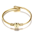 Detail of a golden twisted cable bangle with a heart pendant featuring an engraved letter E - Letter E / Gold