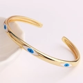 Nahaufnahme der goldenen Evil Eye Manschette mit blauer Emaille auf rosa Hintergrund - 18K Gold / Drei-Augen Klassischer Stil (SL114-5)