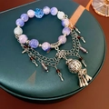 Detail eines Perlenarmbands mit lila Kristallsteinen und silbernen Quastenanhängern - Lila