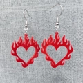 Detalle de pendientes de corazón en llamas de acrílico rojo sobre fondo de tela gris rugosa - Corazón de Llama / Llama Roja