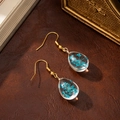 Macro shot of resin drop earrings with blue dried flowers on brown leather surface - Teardrop Style (10399) / Aquamarine