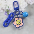 Close-up of blue plastic chain keychain with a yellow smiley face flower and bell charm - 5126-11 Blue Smiling Flower