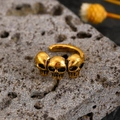 Vintage goldener Ohrclip mit drei Totenköpfen im Punk-Stil auf Stein Hintergrund - Kupfer / Dreifacher Totenkopf / Antikgold