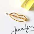 Gros plan d'une pince à cheveux minimaliste dorée en forme de lèvres au design poli - Forme de lèvres