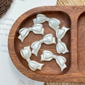 Macro detail of seven white pearlescent resin bow beads for DIY jewelry on a wood tray - White with Bowknot