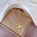 Primer plano de collar con colgante de corazón dorado y pedrería en joyero beige - Estilo Corazón Blanco (E503)