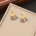 Macro detail of gold hoop earrings with blue evil eye charms on a beige velvet insert - Earrings