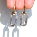 Detail view of 18K gold earrings featuring blue beaded oval drops held by hand - Blue Zircon