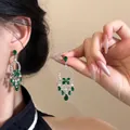 Dettaglio di orecchini a nappa con smeraldi e diamanti e motivi di farfalle e fiori - Stile Fiore con Gemma Verde Incastonata Tonda