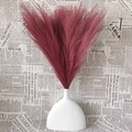 Burgundy artificial pampas grass bouquet in a white ceramic vase on vintage newspaper - Burgundy