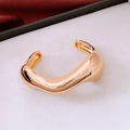 Vista macro de un brazalete abierto dorado con diseño fluido y acabado pulido brillante - Dorado