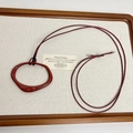 Close-up of red organic shape pendant on long cord displayed on linen board - Red