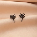 Macro shot of matte black dandelion stud earrings on elegant champagne satin fabric - Dandelion Black