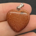 Hand holding a gold sand stone heart pendant with a polished finish and metal bail - 20mm / Gold Sandstone