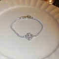 Détail d'un bracelet trèfle argenté serti de zircons cubiques sur porcelaine blanche - Chaîne de Tennis en Forme de Trèfle