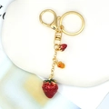 Close-up of a gold metal keychain featuring a red enamel strawberry charm and leaf details - Red Enamel Strawberry