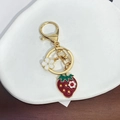 Detalle de llavero de fresa dorada con colgante de flor sobre bandeja de cerámica - Llavero de Fresa