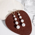 Detailed macro shot of long gold earrings with heart studs and cascading white pearls - Gold Heart Pearl Long Tassel Dangle