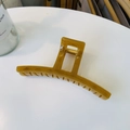 Close-up of amber large shark hair claw clip with strong metal spring on white desk - Autumn Yellow
