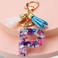 Close-up of letter P resin keychain with colorful stones, golden chain and double tassels - Letter P