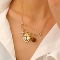 Macro view of gold safety pin pendant with cross, heart, and religious charms on fine chain - 01 KC Gold (0156)