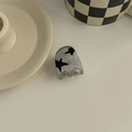 Detail view of a mini silver hair claw with black stars on a checkerboard background - Small