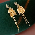 Close-up of golden leaf cluster tassel earrings on deep green velvet display - Gold