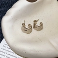 Detailed macro view of gold C-shaped earrings with irregular lava ripple texture on display - Light Coffee Gold