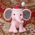 Soft pink plush elephant toy wearing a red plaid Christmas hat on a decorative carpet - Christmas Pink With Red Hat