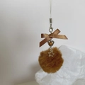 Detail of a brown plush ball charm with a satin bow and heart-shaped metal pendant - Coffee