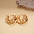 Detailed view of gold metallic hoop earrings with a wavy texture on a stone background - Ear Buckle / Gold