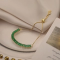 Elegante bracciale placcato in oro con zirconi verdi su sfondo in seta beige - Verde