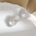 Vista macro di orecchini a cerchio argentati a raggiera su un piatto in ceramica - 24K / Argento