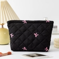 Detailed close-up of a black quilted makeup bag with pink bow embroidery on a vanity - Black