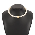 Detailed close-up of a pearl necklace with a polished gold heart pendant on a display - Gold