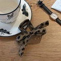 Dettaglio molletta a fiocco tartarugata su tavolo in legno con accessori eleganti - Marrone
