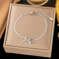 Detail of silver bowknot bracelet with zircon stones on a beige jewelry box display - [B100] Bow Anklet-Steel Color