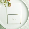 Biglietto di ringraziamento bianco con bordo dorato e scritte verdi su piatto - Stile Grazie