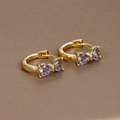 Detailed close-up of 18K gold bow earrings with purple zircon stones on a brown surface - Gold-Purple