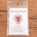 Silver Pocket Hug token with a red enamel heart on a brown wooden background - Vintage Border Enamel Red Heart