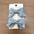 Pair of matte blue grosgrain ribbon bow hair clips displayed on a white product card - Denim Blue
