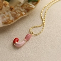 Gros plan d'un collier doré avec pendentif en forme de J rose brillant et détail rouge - Style-J